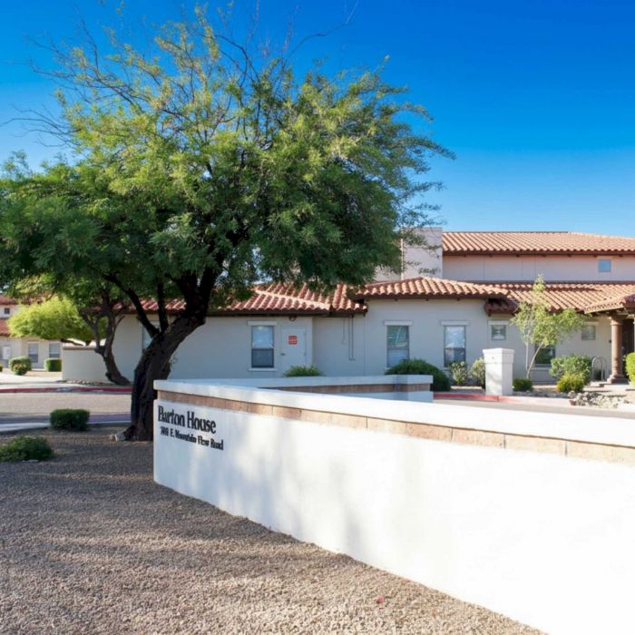 A white stucco building with a red tile roof and a sign reading "Barton House" in a landscaped area.