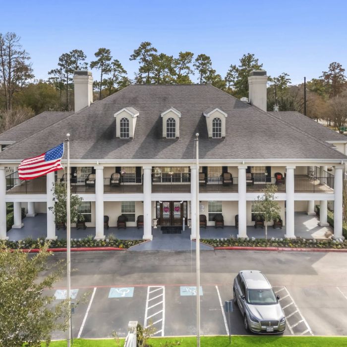 The Tarina of Cypresswood is a large two-story building with columns, an American flag, and parked cars in front on a sunny day.