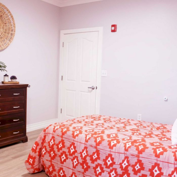 Bedroom with a red and white patterned bedspread, dresser, and wall decor in a softly lit room.