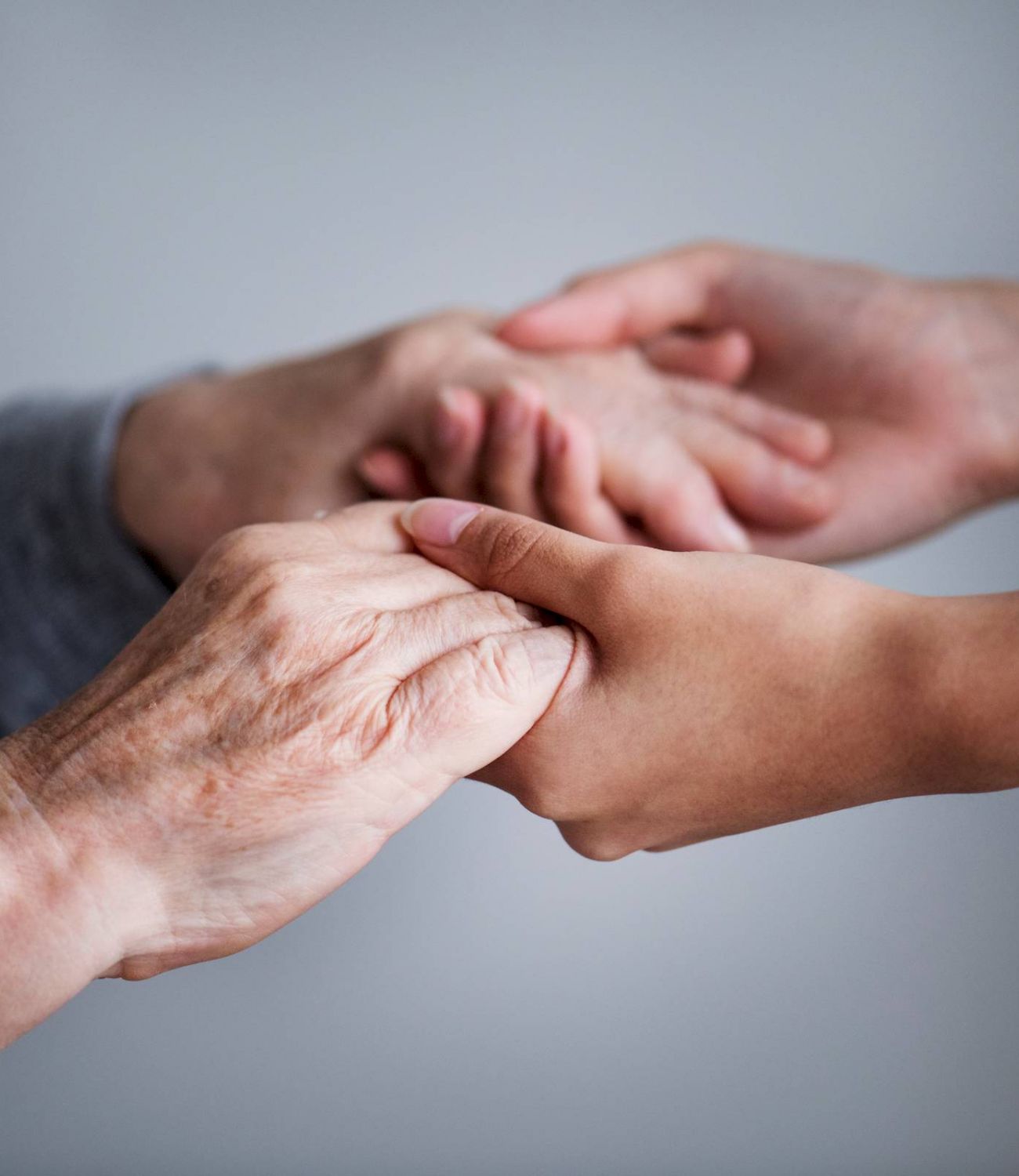 Close-up of young and elderly hands gently holding each other against a neutral background.