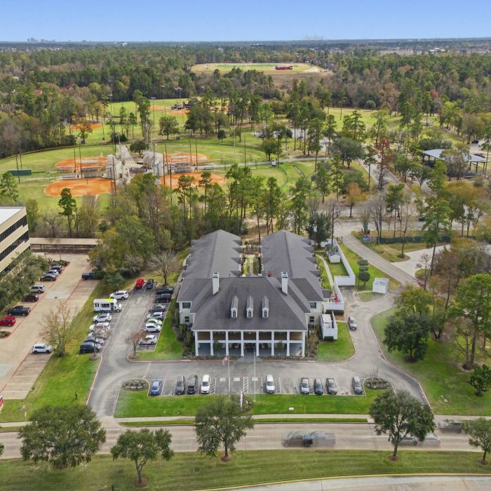Aerial view of Tarina of Cypresswood, showcasing its large building, parking lots, and sports fields amid lush trees and greenery.