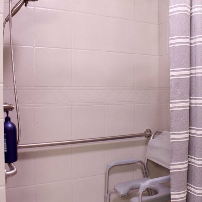 Accessible shower with a shower chair, grab bar, handheld showerhead, and striped shower curtain.