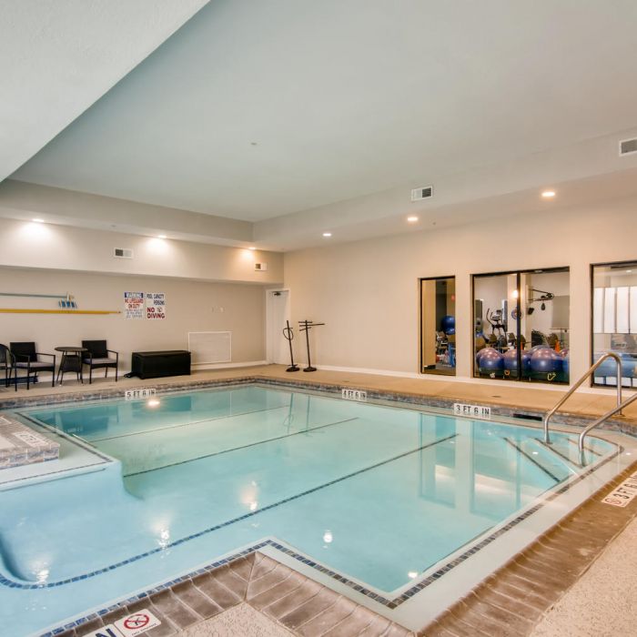 Indoor swimming pool with chairs, exercise balls, and beige walls in The Terraces at Kingwood senior living’s bright, inviting space.