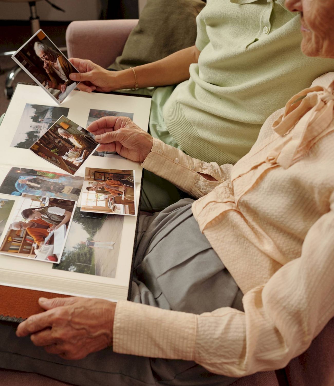 Two people sit together on a couch at Barton House, looking through a photo album and holding old photographs.