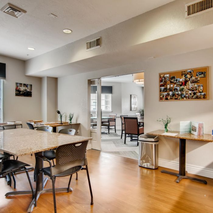 Bright community room with tables, chairs, and wood flooring at The Terraces at Kingwood, leading to a connected space for gatherings.