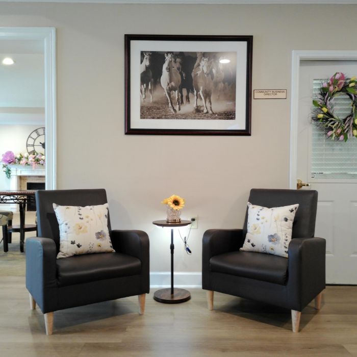 Two armchairs with floral pillows, a table with a sunflower, and a Tarina of Kingwood horse photo on the wall above.