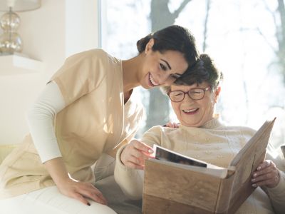 A memory care resident smiles as she looks through a photo album with a caregiver.
