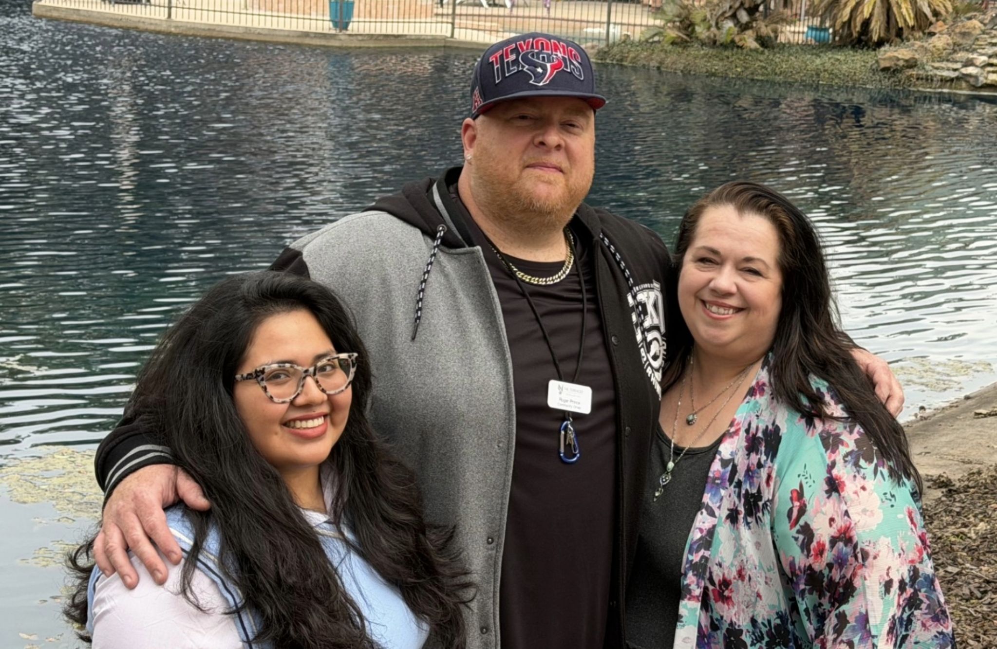 Three people smiling by a pond, honoring every story and remembering ours among the trees and rocks in the background.