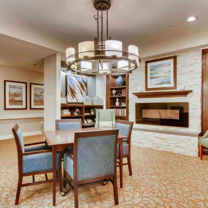 Modern lounge at The Terraces at Kingwood with blue chairs, wooden table, fireplace, bookshelves, and wall art under warm lighting.