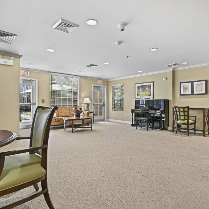 Spacious Tarina of Cypresswood lounge with tables, chairs, a couch, piano, and large windows letting in natural light.