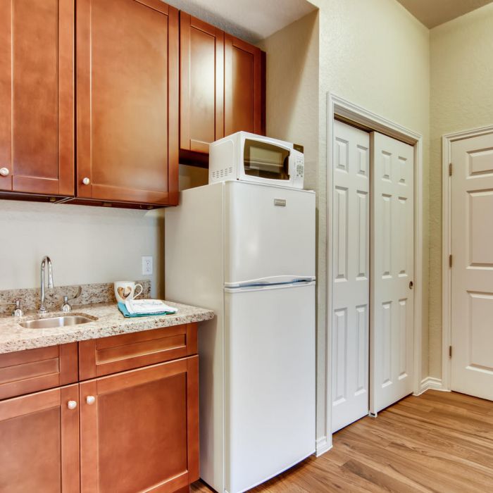 Small kitchen area with brown cabinets, white fridge, and microwave—ideal for comfortable living at The Terraces at Kingwood.