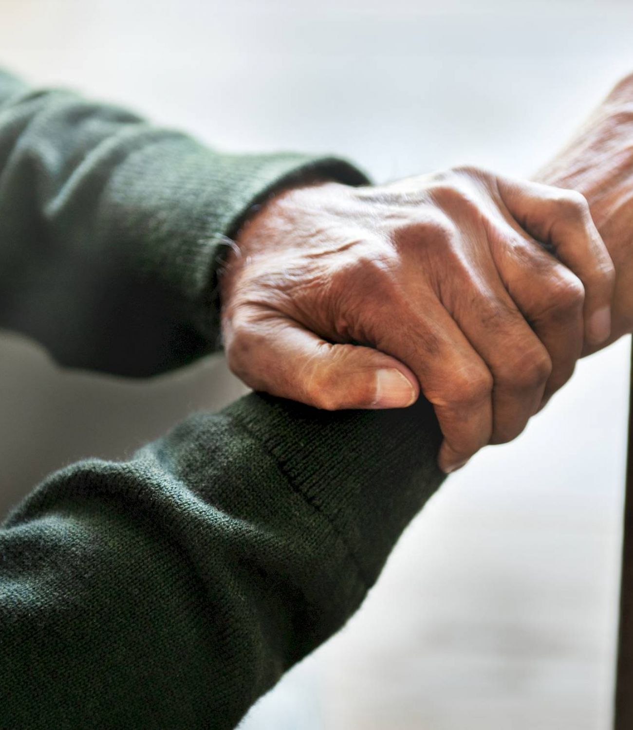 Close-up of elderly hands resting on a cane, wearing a dark green sweater.