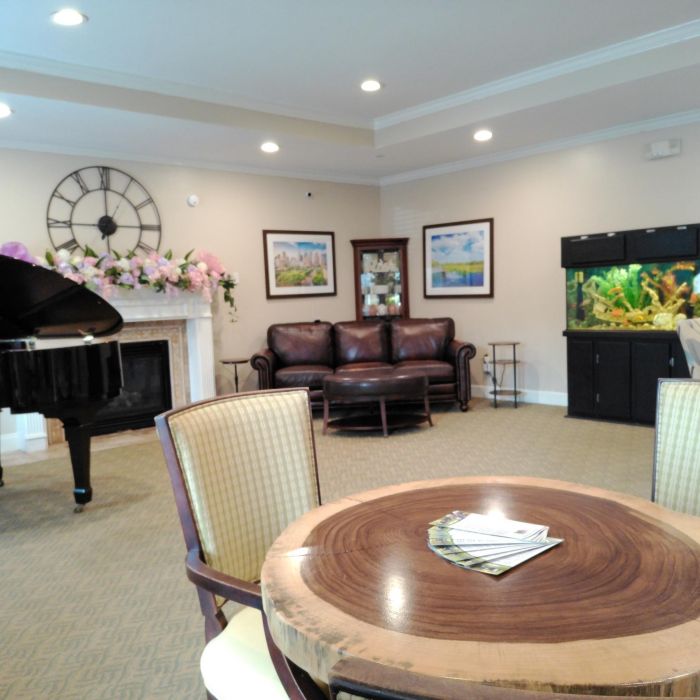 A cozy Tarina of Kingwood living room with a grand piano, sofa, fish tank, and a round table with chairs and magazines.