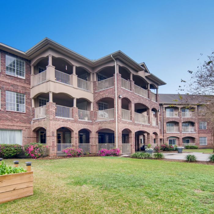 Three-story brick apartment at The Terraces at Kingwood with balconies, courtyard, and raised garden beds—perfect for senior living.