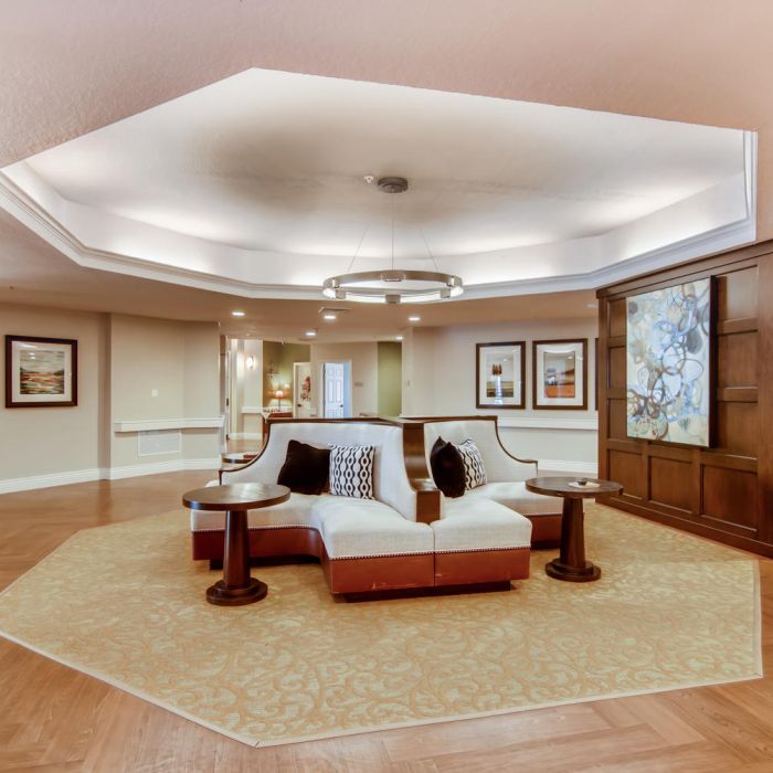 Spacious lobby at Terraces at Kingwood with sectional sofa, art-filled walls, and warm tray ceiling lighting for inviting senior living.