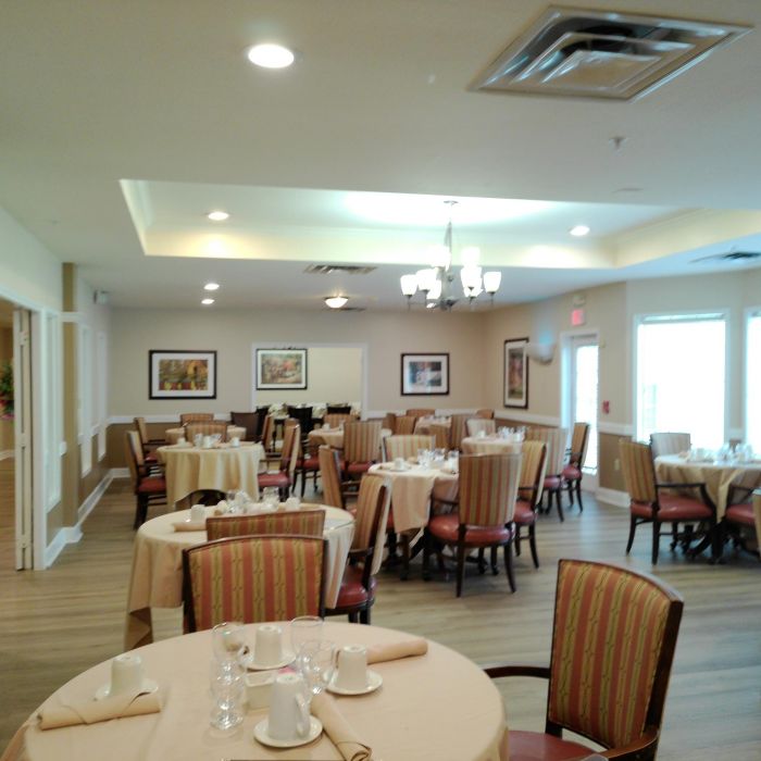 A dining room at Tarina of Kingwood with round tables, striped chairs, and large windows letting in natural light.