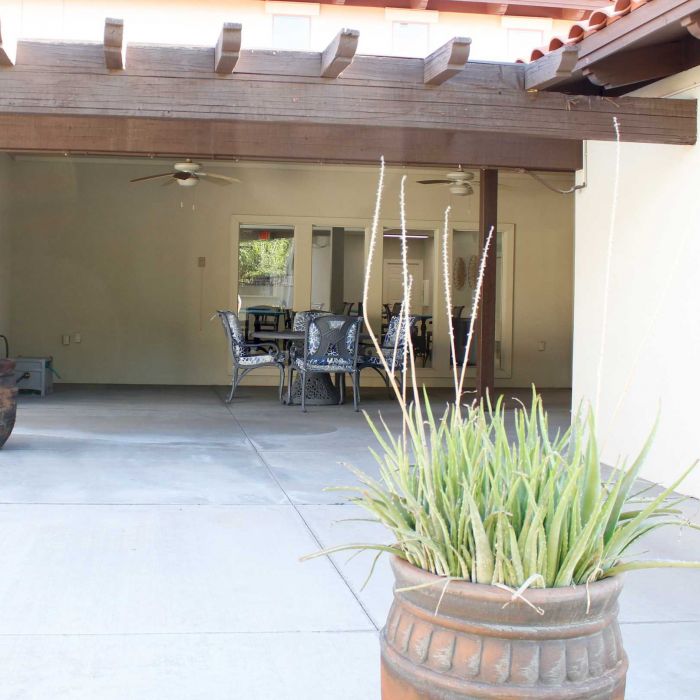Covered patio with outdoor dining set, ceiling fans, and potted plants on a concrete floor.