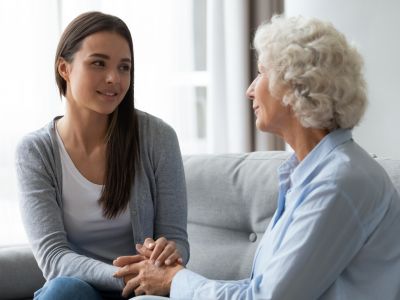 Younger woman holding an older woman's hands while they sit across from each other at a kitchen table