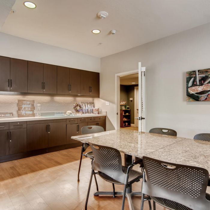 Modern kitchen at The Terraces at Kingwood with dark cabinets, granite table, black chairs, wood floor, and wall art.