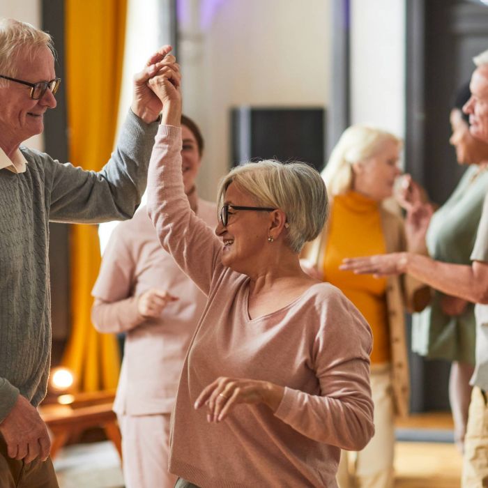 Seniors smiling and dancing together at a social gathering indoors.