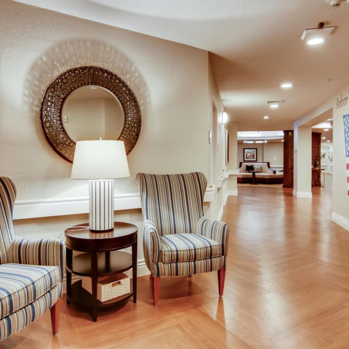 Two striped armchairs by a round table and lamp, near a wall with a mirror and patriotic decor at Terraces at Kingwood.