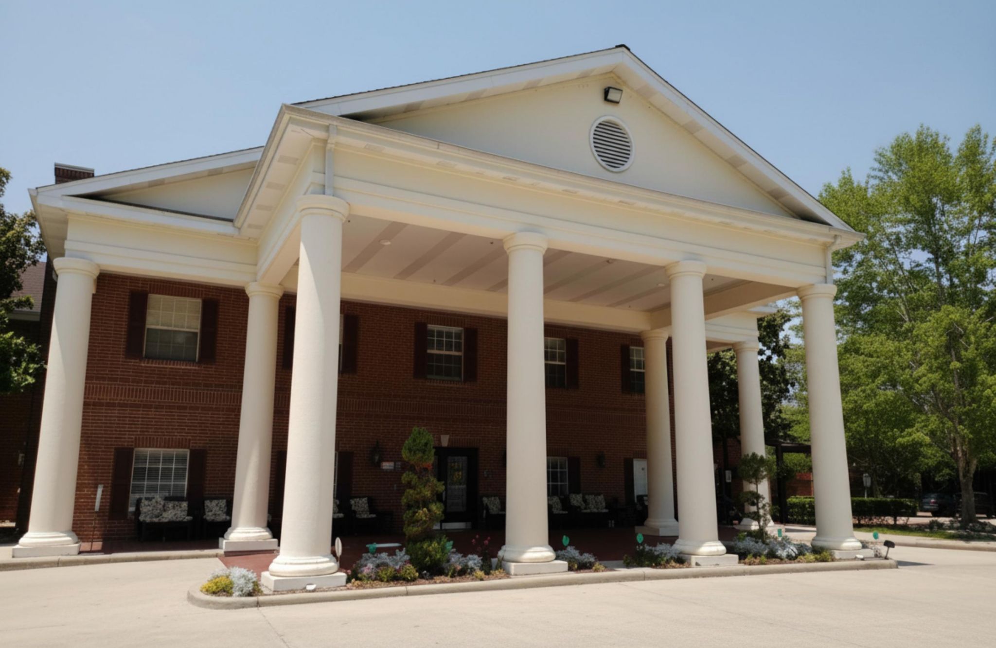 A brick building with large white columns at the entrance and flowers along the walkway at Tarina of Kingwood.
