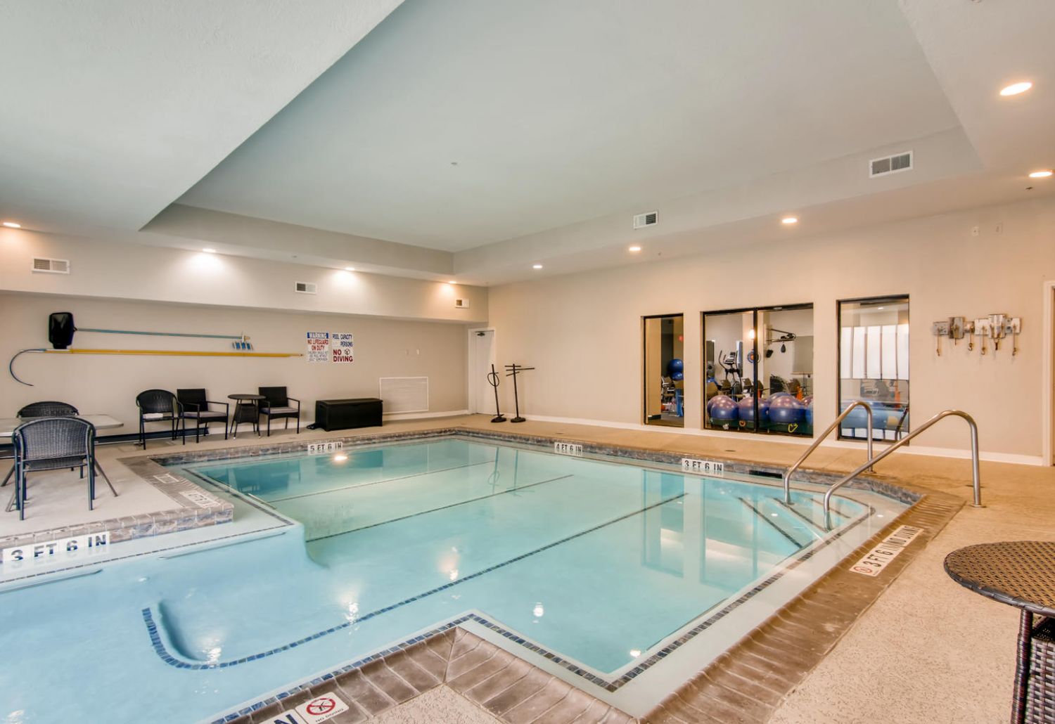 Indoor swimming pool with chairs, exercise balls, and beige walls in The Terraces at Kingwood senior living’s bright, inviting space.