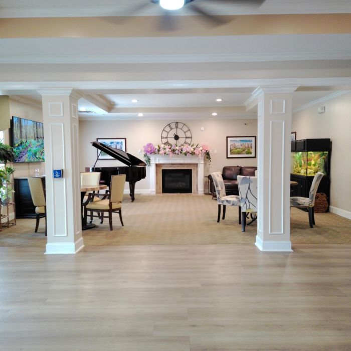 Spacious, elegant living room at Tarina of Kingwood with a grand piano, fireplace, art, and flowers adorning the seating areas.
