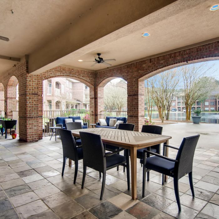 Covered patio with tables, chairs, brick arches, and scenic views at The Terraces at Kingwood assisted living Kingwood.