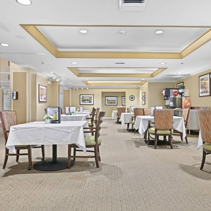 Spacious, well-lit dining room at Tarina of Cypresswood with tables set for four, white tablecloths, and wicker chairs.