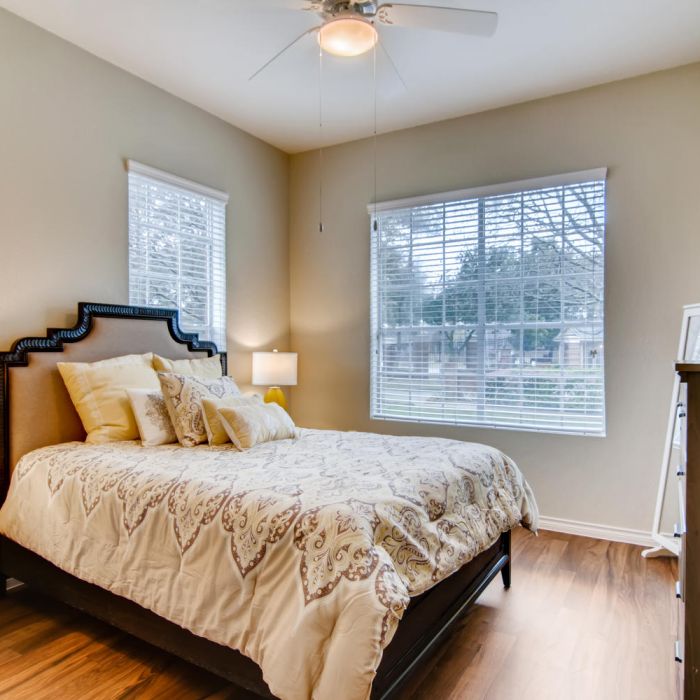 Bright bedroom at Terraces at Kingwood features yellow accents, large windows, wooden floors, and a ceiling fan—perfect for senior living.