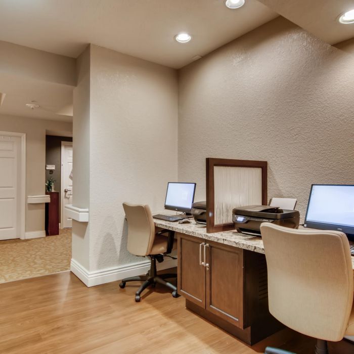Two computer workstations with printers and chairs in a well-lit, carpeted office at Terraces at Kingwood senior living.