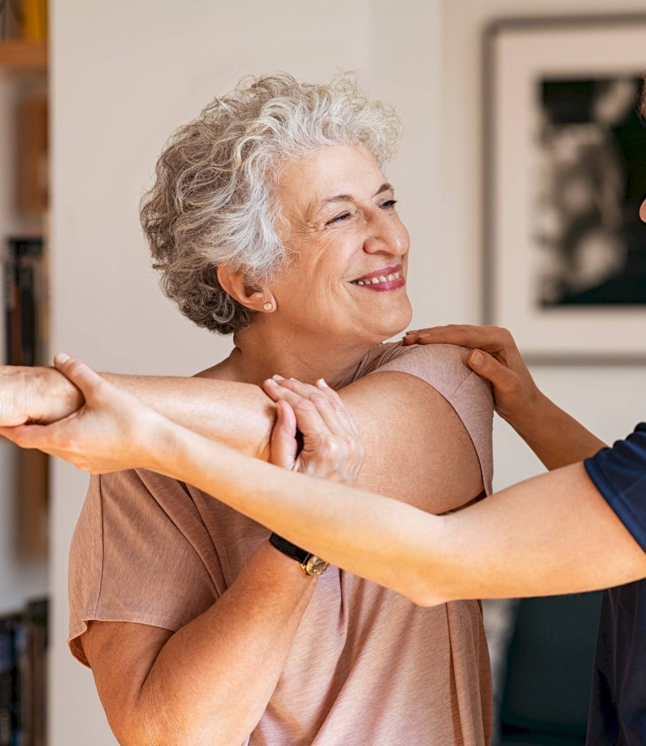 Elderly woman smiling while her Tarina of Kingwood caregiver helps her stretch her arm at home.