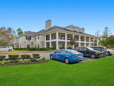 Two-story white Cypresswood homes with columns, landscaped lawn, and parked cars on a sunny day.
