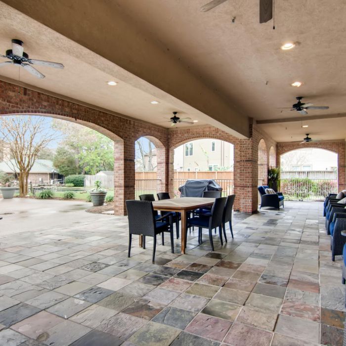 Covered patio with tile floor, ceiling fans, stylish seating, and brick arches overlooking the yard at The Terraces at Kingwood senior living.