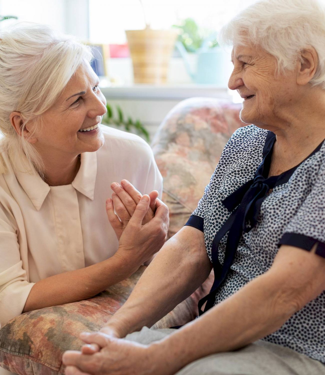 Smiling woman sits beside and talks with an elderly woman in the cozy, well-lit living room at Barton House.