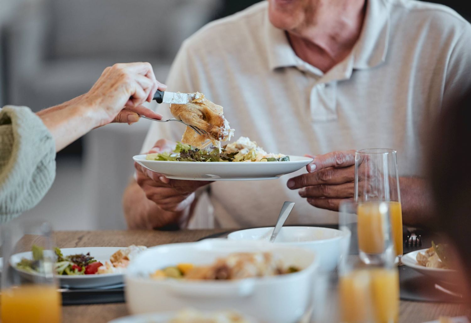 Two people serving food onto a plate at a table set with dishes and glasses of orange juice.