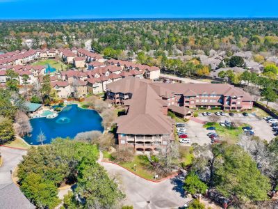 Aerial view of The Terraces at Kingwood, a senior living complex with a pond, fountain, parking lot, and lush surrounding trees.