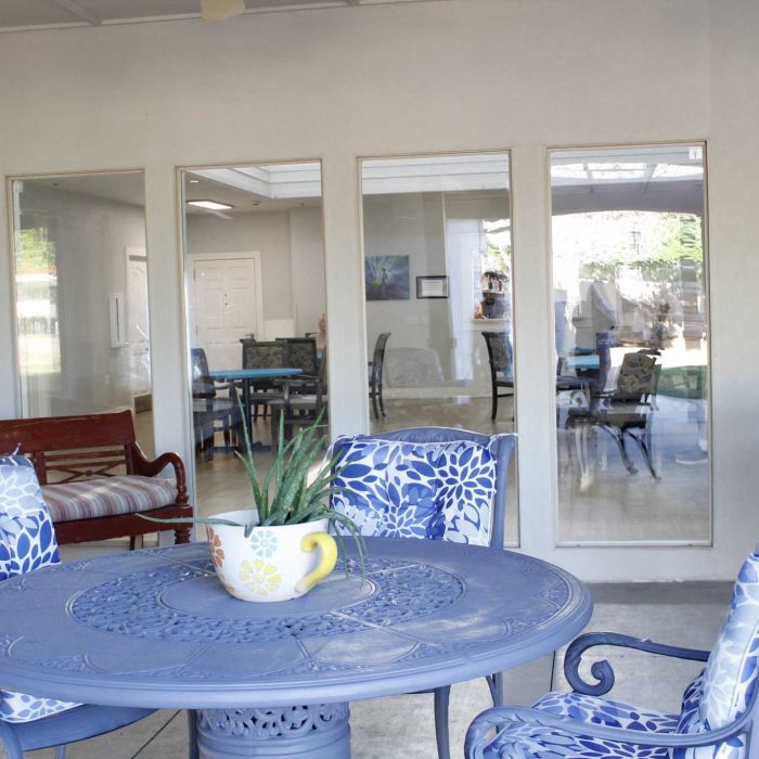 Blue patio table and chairs with a potted plant, seen outside a room with glass doors and indoor seating.