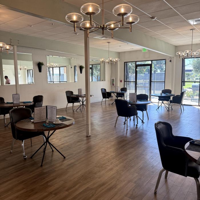 Bright, modern dining area at Tarina of Stockton with round tables, black chairs, wood flooring, and sunlit large windows.