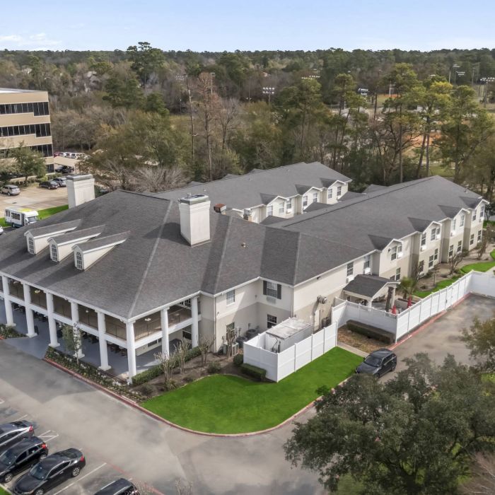 Aerial view of Tarina of Cypresswood, a large residential building with a parking lot and trees surrounding the property.