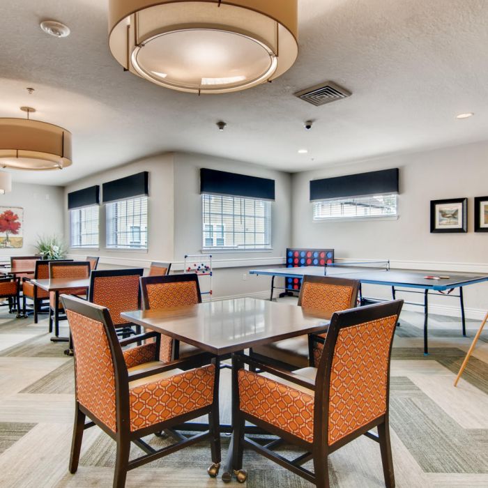 A bright game room at The Terraces at Kingwood features tables, chairs, a ping pong table, board games, and wall art for senior living fun.