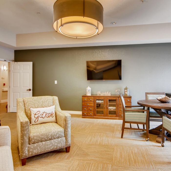 Cozy living room at Terraces at Kingwood with armchair, TV, dining table, and warm lighting—perfect for assisted living in Kingwood.