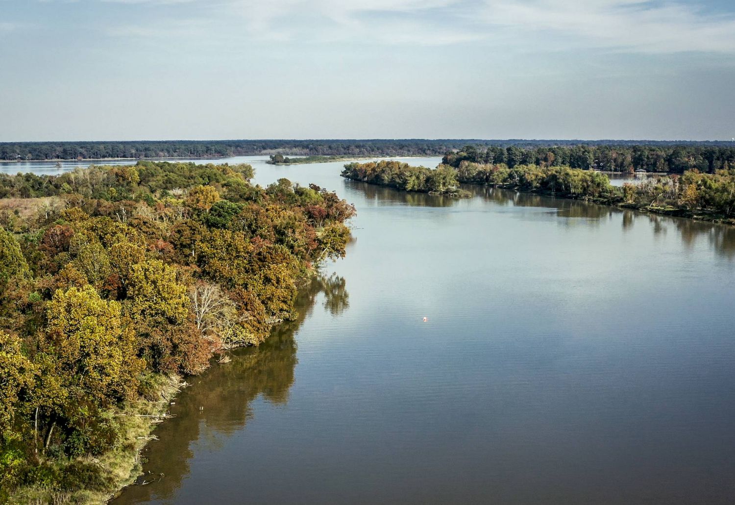 Houston Lake, a wide river winding through dense, green forests under a partly cloudy sky in the tranquil Tarina of Kingwood.
