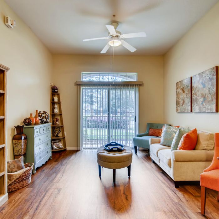 Bright living room with wood floors, cozy seating, and large window—perfect for senior living at Terraces at Kingwood.