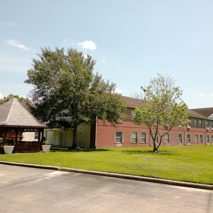 A red-brick two-story building at Tarina of Kingwood, featuring a gazebo and trees on a sunny day.