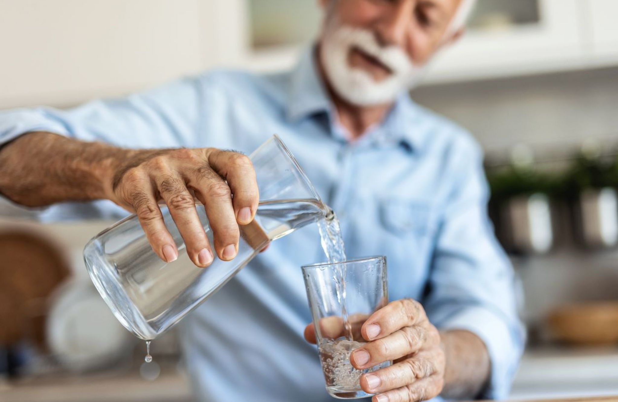 An older man pours a refreshing glass of water in his kitchen to hydrate himself.