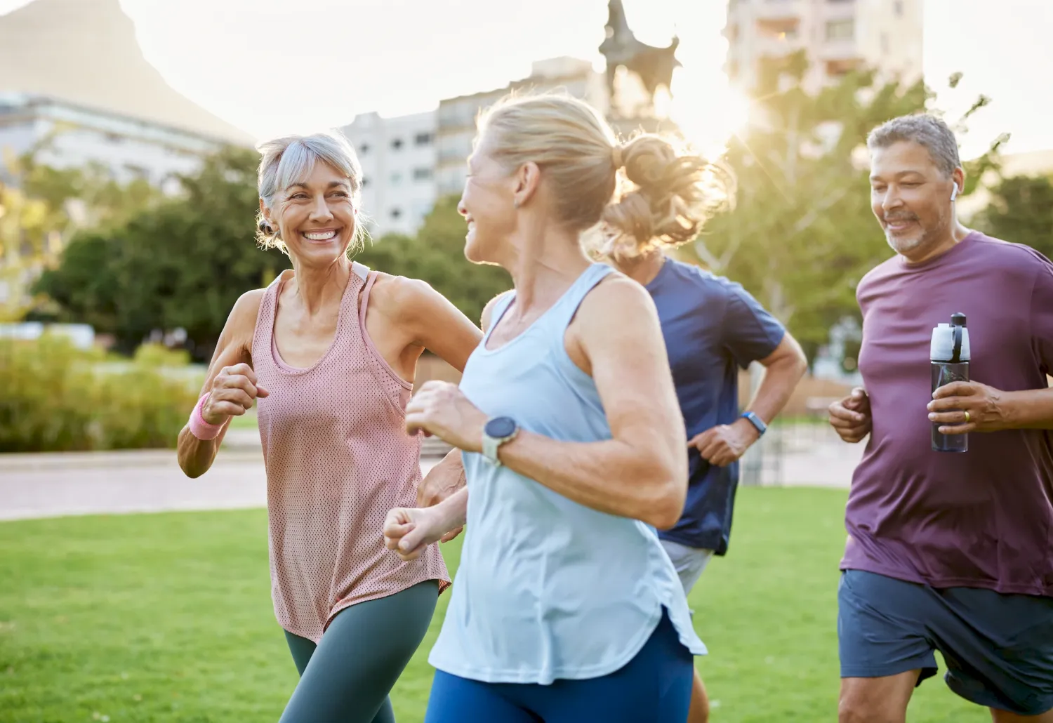 Four adults jogging together in a park, smiling and enjoying outdoor exercise on a sunny day.