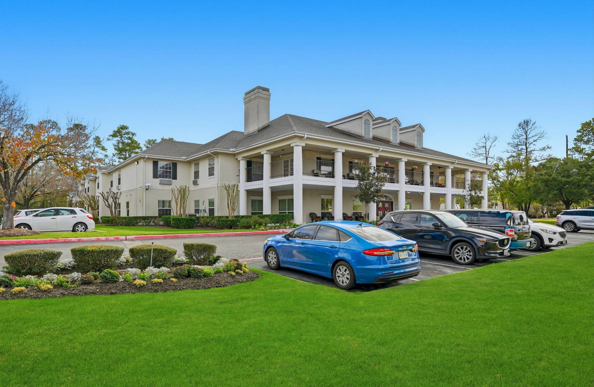 Two-story white Cypresswood homes with columns, landscaped lawn, and parked cars on a sunny day.