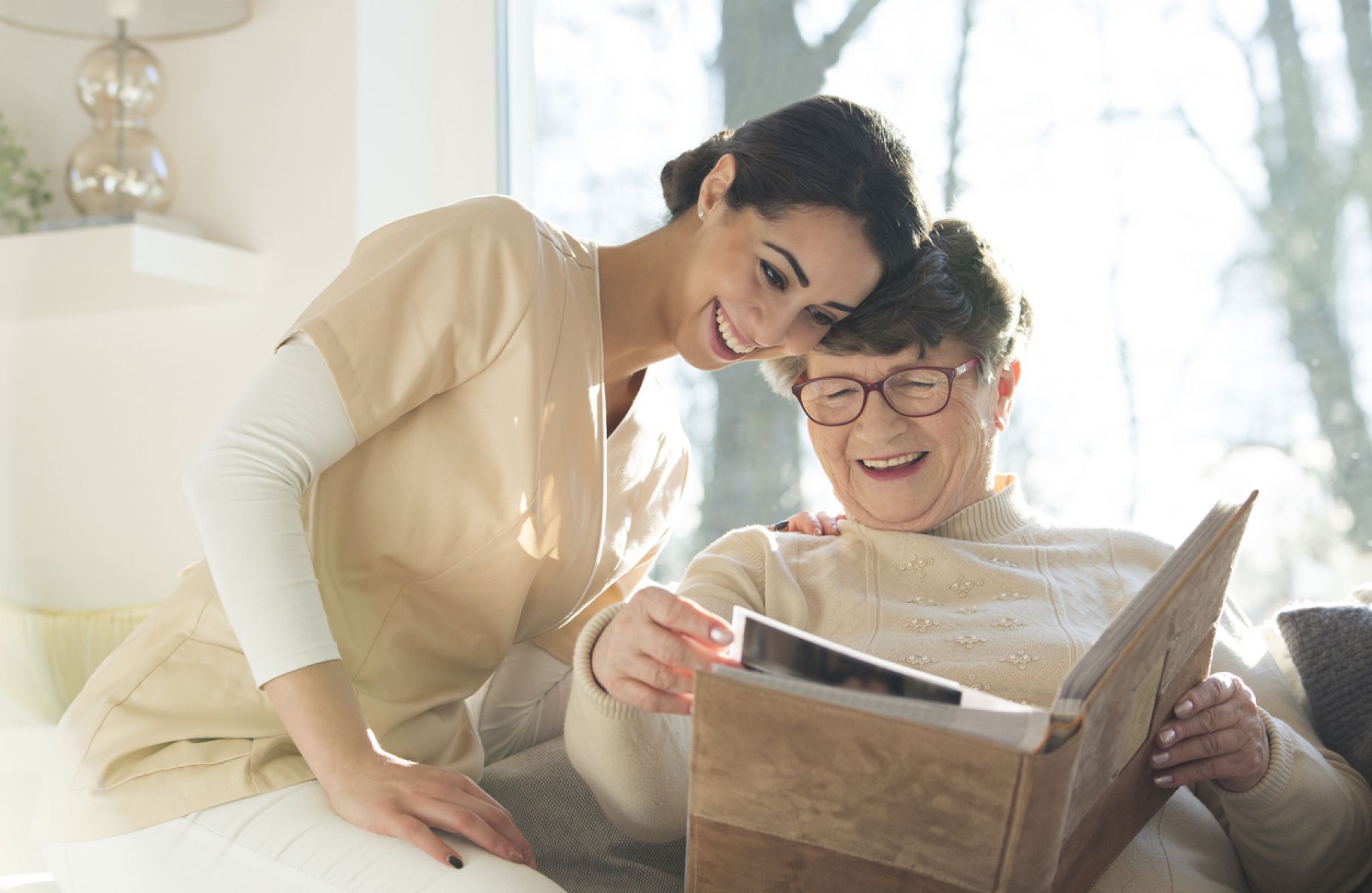 A memory care resident smiles as she looks through a photo album with a caregiver.